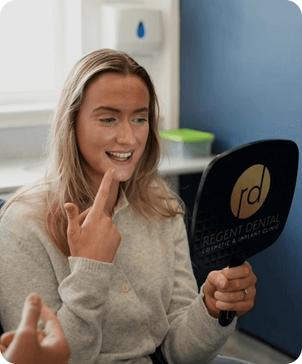 A patient smiling and checking her teeth in a hand mirror